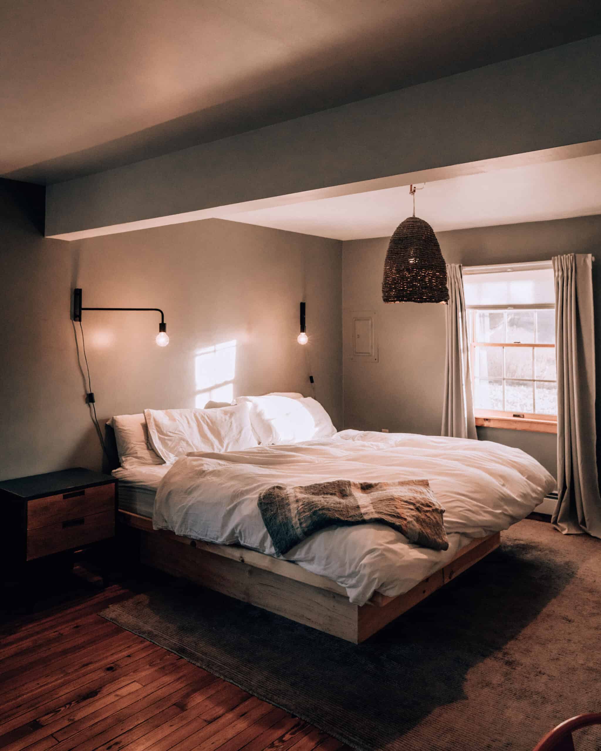 Cozy rustic bedroom with boho ethnic decor. Large windows. Double wooden bed  with many pillows and handmade textiles. Wooden furniture. Plants in the  interior. Nobody. Large windows in appartment. Stock Photo