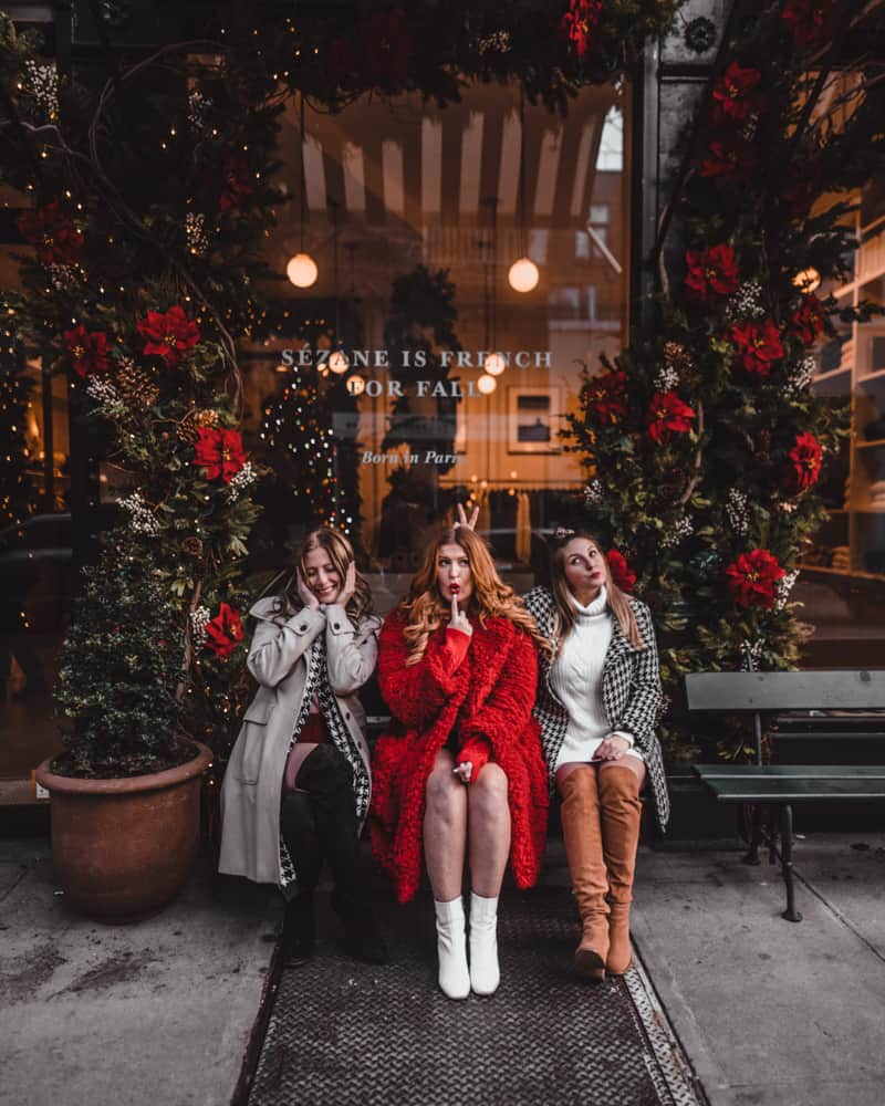 3 girls sitting on a bench outside of a boutique shop